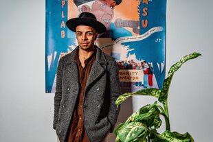 Der Schwarze Aktivist Zefanias M. steht vor einem Plakat, dass die Antirassismus-Koryphäe Biplab Basu zeigt