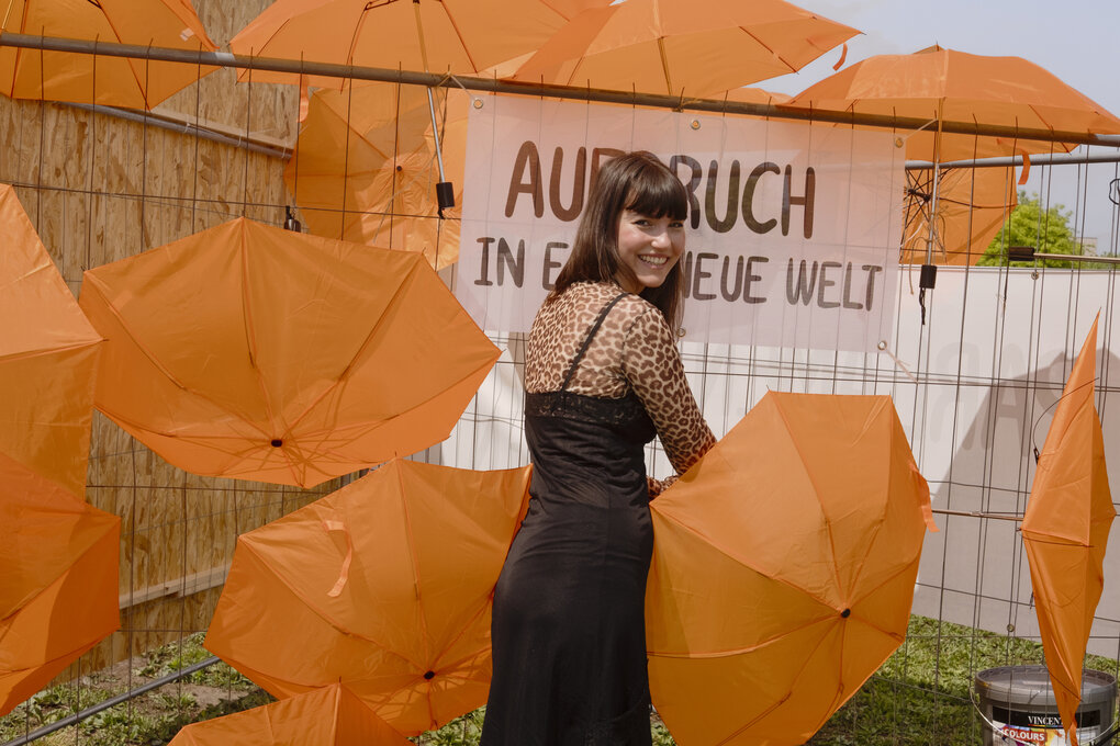 Porträt Carla Hinrichs inmitten von orangefarbenen Regenschirmen