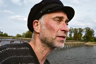 Der Schauspieler Andreas Uehlein steht vor einem Fluss.